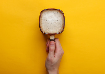 Wall Mural - Hands holding cup of latte or cappuccino on yellow background. Coffee with milk. Top view