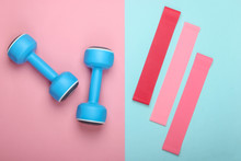 Dumbbells With Fitness Elastic Bands On Pink Blue Pastel Background. Top View, Flat Lay
