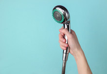 Hand Holds A Shower Head On Blue Background.