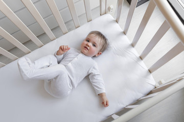 A cute little girl is smiling as she lies in her children's bed with white sheets. Space for text. On a white background with a copy of the space. Cute little baby lying on the bed, top view.