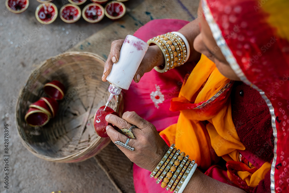 Indian woman in traditional costume decorating and painting a small clay bowl  - obrazy, fototapety, plakaty 