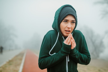 Wall Mural - Close shot of young girl in warm sportswear trying to warm up her hands before starting with running session on cold day.