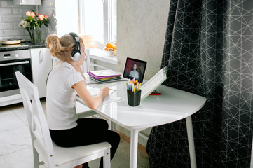 Teen girl school pupil wears headphones conference calling studying online with remote tutor from home. Teenage student using laptop talking in webcam video chat learning lesson with distance teacher.