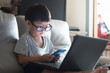 © Eaknarin - little boy Wear glass using laptop on sofa in home, work from home