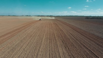 Wall Mural - Tractor in the dust working in the field. Tractor with a modern sowing seeds machine in a newly plowed field. Plowed land as a background. Two red tractors on the field.
