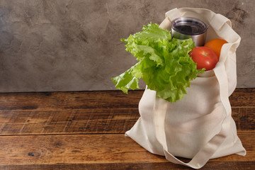 Eco-friendly groceries bag. Reusable shopping bag with fresh fruits and greens on wooden background. Bag , green salat, orange , tomatos on brown table. Healthy food, useful organic products.