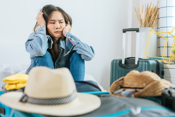 Quarantine, young asian pretty woman traveler upset after flight cancelled with packing clothes into suitcase for vacation on bed at home, delay flight, summer holiday, backpacker and travel concept