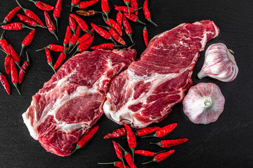 Fresh steaks from Raw pork meat on dark stone background, garlic and pepper. Top view, food concept