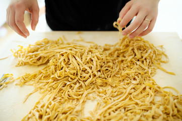 Staying at home with your family and preparing fresh home-made pasta (tagliatelle): mom moving pasta noodles on a wooden board and mixing with flour.