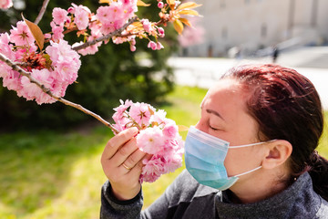 The girl in the park sniffs a sakura flower in a protective mask. A woman walks in a sakura park.Outdoor.