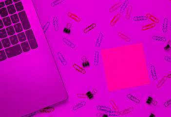 Wall Mural - Minimalistic office still life. Laptop, stationery (paper clips, felt-tip pen, memo piece of paper) in pink neon light. Studio shot.