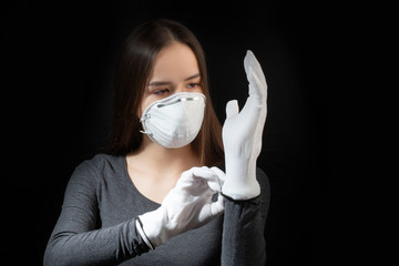 Poster - Coronavirus protection. Young woman in a white antibacterial medical mask puts on gloves on a black background