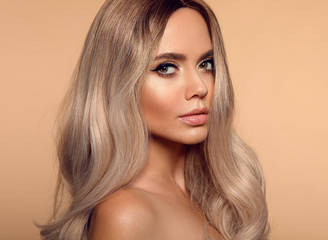 Wall Mural - Ombre blond wavy hairstyle. Beauty fashion blonde woman portrait. Beautiful girl model with makeup, long healthy hair style posing isolated on studio beige background.