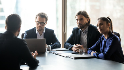 Wall Mural - Three interested attentive hr managers listening to candidate on interview, sitting at table in boardroom, applicant seeker answering recruiters questions, colleagues looking at mentor coach