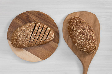 Two loaves of bread with seeds and flakes on wooden cutting boards on white background.