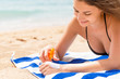 © sosiukin - Cute and smiling woman is applying sunscreen on her hand with the finger sunbathing on the towel at the beach