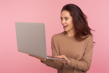 Wall Mural - Portrait of surprised freelancer working on computer. Amazed young woman in casual sweater reading shocking message on laptop, working or studying online using computer. indoor studio shot isolated