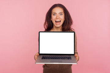 Wall Mural - Portrait of surprised woman holding laptop with white screen copy space, mock up display for internet advertising, shocked by online service, expressing amazement. indoor studio shot, pink background