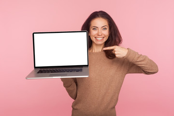 Wall Mural - Portrait of cheerful woman pointing at laptop with white screen copy space, mock up display for internet advertising, online service, website promotion. indoor studio shot isolated on pink background
