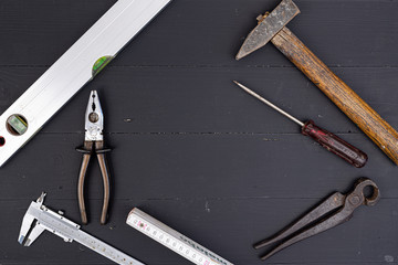 Old used hammer, pliers, libella, measuring meter, nonius and screwdriver with copy space on the black wooden board table. Do it yourself DIY concept with hand tools in top view mode