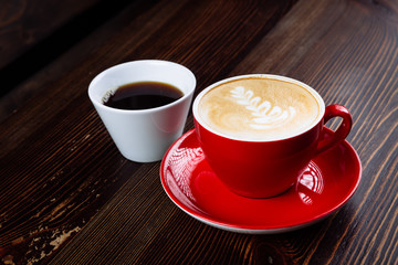 Coffee in a red cup with milk and latte art and coffee in a white cup on a table