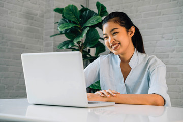 Wall Mural - Happy friendly Asian woman using a laptop and talking, making video call conference, online job interview at home. Millennial female internet teacher tutor and vlogger working from home on the job.