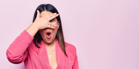 Sticker - Young beautiful business woman wearing elegant jacket standing over pink background peeking in shock covering face and eyes with hand, looking through fingers afraid