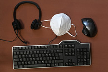 Smart Working During Covid-19 Or Coronavirus Disease. Computer Keyboard, Mouse, Headphone, And Protection Mask Ffp2 Against Covid-19 On A Brown Background.
