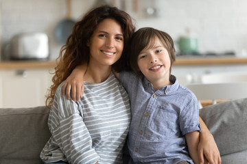 Happy little child boy embracing elder sister, portrait. Head shot young woman nanny babysitter cuddling small kid, looking at camera. Attractive single mother posing for family photo with son.