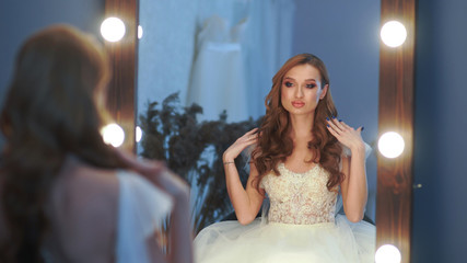 Beautiful girl model in wedding dress posing in front of a mirror.