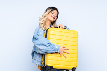 Traveler teenager holding a suitcase isolated on blue background in vacation with travel suitcase