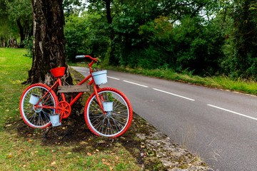 A picturesque and beautiful red ornament bicycle on a tree by the side of a road