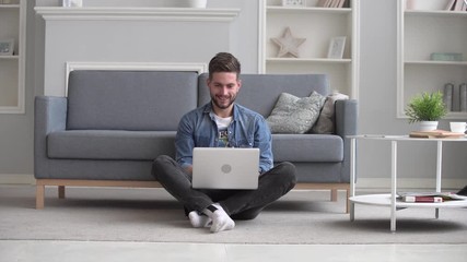 Wall Mural - Young man seat on carpet in living room and use laptop. Man use laptop for working at home or watching video in social network.