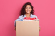 © sementsova321 - Closeup portrait of happy caucasian brunette woman holding carton box with donation, adorable female posing isolated over pink studio background, dark haired girl looking directly at camera.