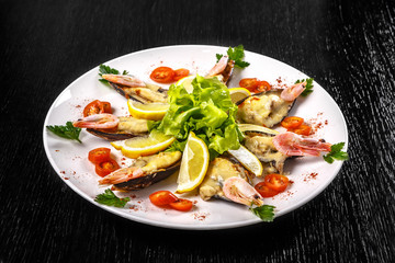 Wall Mural - Shrimps, tomatoes and lemon are beautifully laid out on a dish on a black background.