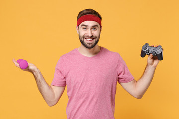 Poster - Smiling young bearded fitness sporty guy 20s sportsman in headband t-shirt in home gym isolated on yellow wall background. Workout sport motivation concept. Spreading hands with dumbbell and joystick.