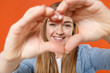 © ViDi Studio - Smiling young woman girl in casual denim clothes posing isolated on orange background studio portrait. People lifestyle concept. Mock up copy space. Showing shape heart with hands, heart-shape sign.