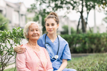 Wall Mural - Nurse caregiver embracing happy Asian elderly woman outdoor in the park. Focused on eldery woman