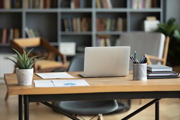 wooden work desk with laptop and documents, books, modern interior of cozy cabinet, table for busine