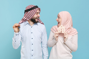 Canvas Print - Excited couple friends arabian muslim man wonam in keffiyeh kafiya ring igal agal hijab clothes isolated on blue background. People religious concept. Hold house bunch of keys, looking at each other.