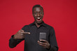© ViDi Studio - Excited young african american man guy in classic black shirt posing isolated on red background studio portrait. People lifestyle concept. Mock up copy space. Pointing index finger on mobile phone.