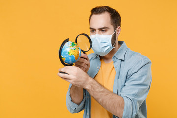 Sticker - Young man in sterile face mask posing isolated on yellow wall background in studio. Epidemic pandemic coronavirus 2019-ncov sars covid-19 flu virus concept. Look throw magnifying glass on world globe.