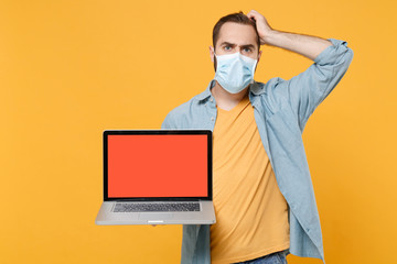 Sticker - Preoccupied man in face mask isolated on yellow background. Epidemic pandemic coronavirus 2019-ncov sars covid-19 flu virus concept. Hold laptop pc computer with blank empty screen, put hand on head.