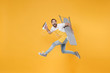 Side view of excited young man househusband in apron rubber gloves hold iron board for ironing while doing housework isolated on yellow background studio. Housekeeping concept. Jumping looking camera.