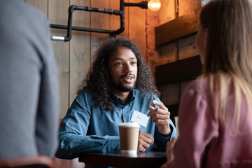 Multiracial young people sit in cafe engaged in speed dating experience chatting and talking, happy diverse multiethnic men and women have fun meeting in coffeehouse for conversation