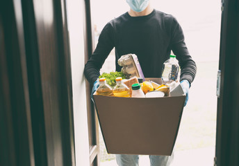 The courier is delivering the cardboard eco box with groceries from the supermarket wearing latex gloves and medical mask