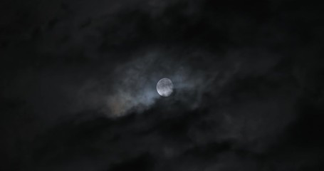 Wall Mural - moon shot behind dark clouds moving at night in real time