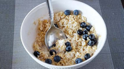 Wall Mural - man eats delicious oatmeal cereals with blueberries and milk for breakfast at home close-up