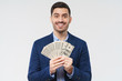 © Damir Khabirov - Young businessman feeling happy about getting increased income and receiving profit from new startup, holding dollars in cash in hands, smiling, isolated on gray background