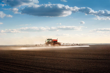 Fototapete - self-propelled sprayer with long arms disperses fertilizers on agricultural fields, rear view, backlit jet